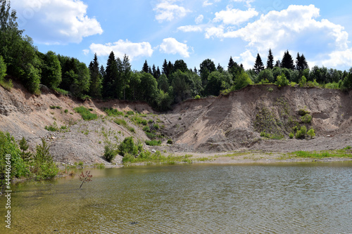 Flooded quarry. Sandy hills, blue sky, water and trees. Summer sunny landscape. Beautiful nature. Lake in the park.