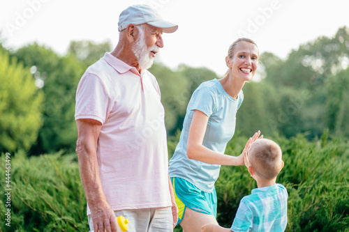 Summer, sport, outdoor activities concept. Happy and cheerful grandfather walking outdoor with his daughter and grandson. Portrait of multi generation family spending time together in park.