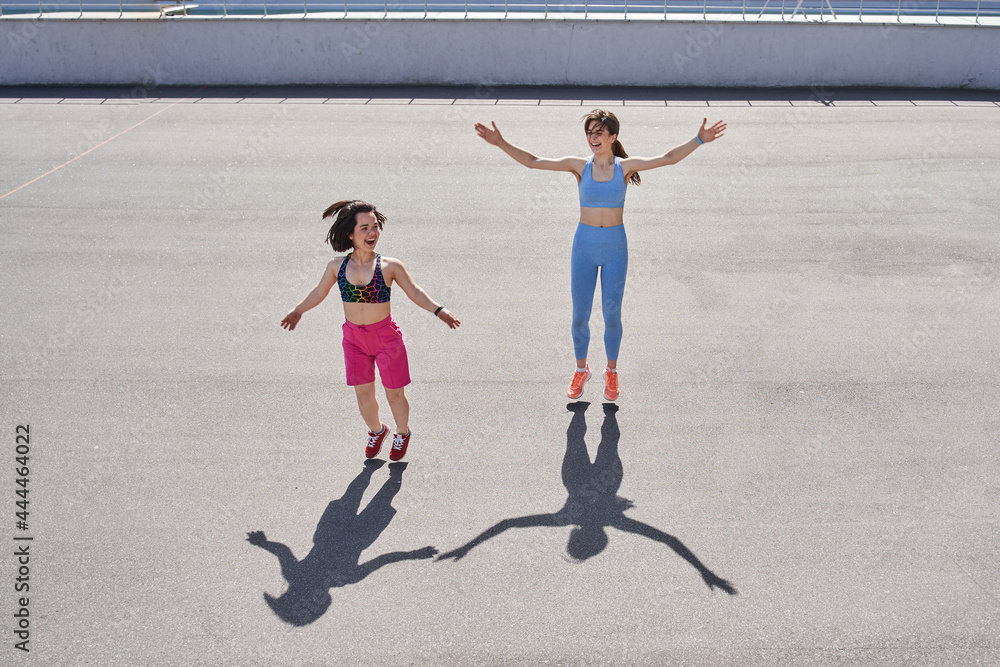 Two diverse girls jumping at the track at the stadium while having their morning workout Two diverse girls jumping at the track at the stadium while having their morning workout