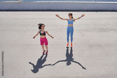 Two diverse girls jumping at the track at the stadium while having their morning workout