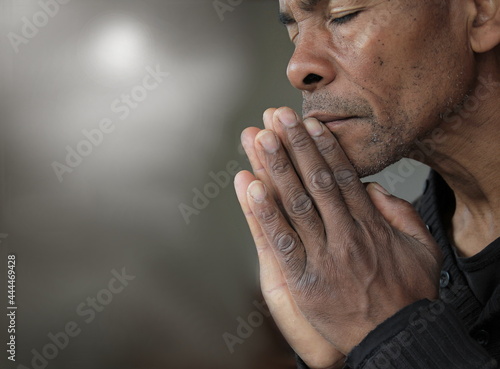 man praying to god Caribbean man praying with hands together stock photo