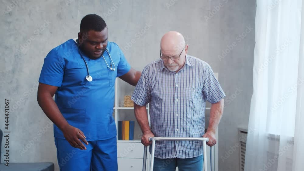 African-American caregiver is teaching disabled old man to walk with walker. Professional nurse and handicapped patient in a nursing home. Assistance, rehabilitation and health care. African-American caregiver is teaching disabled old man to walk with walker. Professional nurse and handicapped patient in a nursing home. Assistance, rehabilitation and health care.