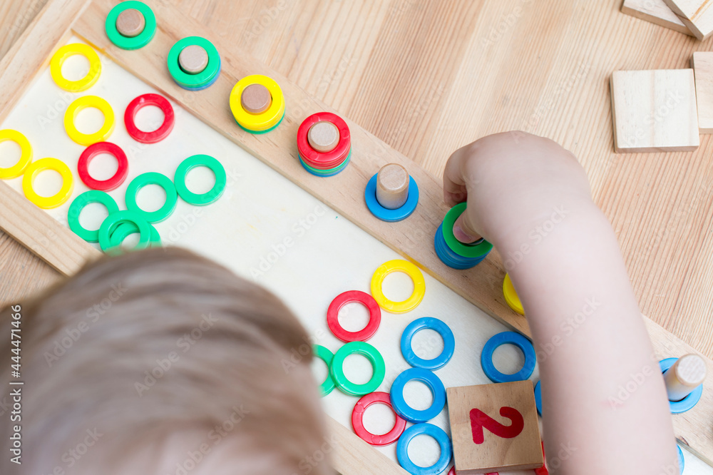 Child playing with different color wooden rings. Sequence, fine motor skills, therapy task for education and brain exercise. Counting math play game. Montessori type implement. Wooden toys. Child playing with different color wooden rings. Sequence, fine motor skills, therapy task for education and brain exercise. Counting math play game. Montessori type implement. Wooden toys.