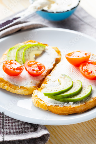 Avocado toasts with cream cheese on a white plate. Toasts with avocado and cherry tomatoes on a linen napkin. Healthy food. Close-up