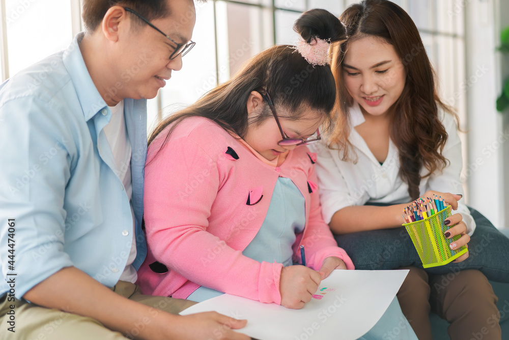 Obraz premium Happy asian family sitting on sofa and together paint with their daughter down syndrome child in living room at morning time, Activity happy family lifestyle concept,