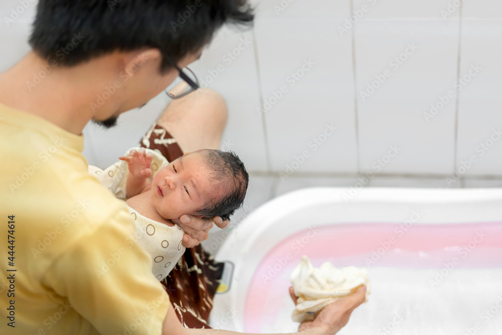Asian father give a bath newborn baby in a tiny bathtub in bathroom. Asian father give a bath newborn baby in a tiny bathtub in bathroom.
