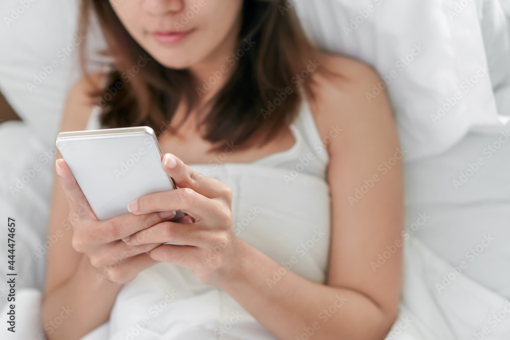 Young asian woman playing with her smathphone on white pillow on bed in bedroom on morning time after wake up, Selective focus. Young asian woman playing with her smathphone on white pillow on bed in bedroom on morning time after wake up, Selective focus.