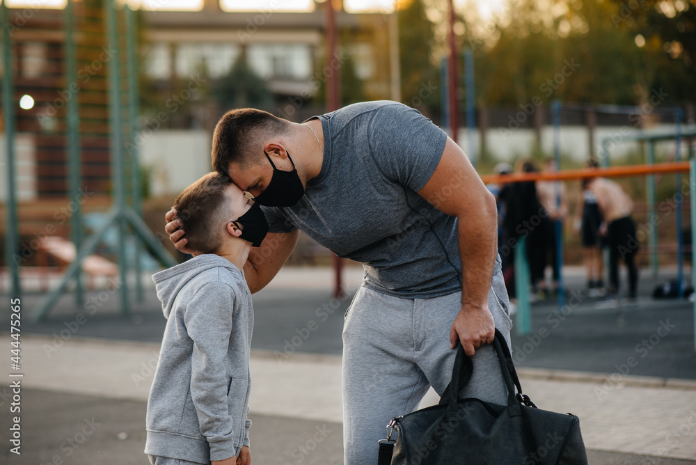 A father and child stand on a sports field in masks after training during sunset A father and child stand on a sports field in masks after training during sunset