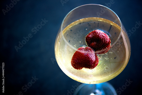 Top view on glass of chilled white wine with strawberries on blue pool water background