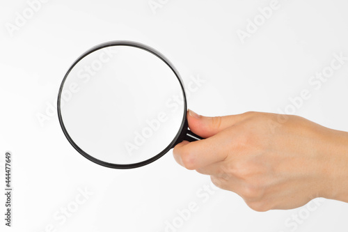 Magnifying glass in hand. Magnifier on a white background. Copy space under magnifying glass. A woman's hand increases something. It will syvolize search or exploration. Blank magnifying glass