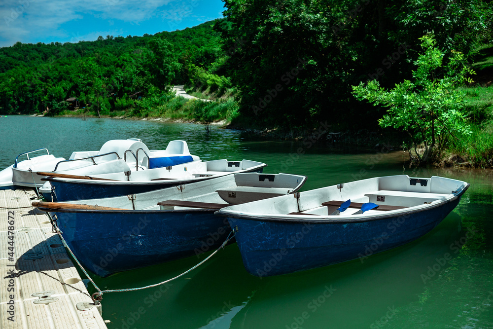 Several rowing boats on the shore of a beautiful lake. Rowing boats in turquoise water on a background of a forest in sunny weather.