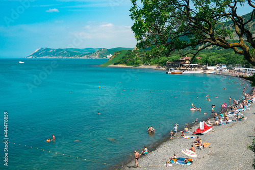 Beautiful coast of the Black Sea with a crowd of tourists on a background of green hills. The beach with many tourists resting in the sun with hot weather.