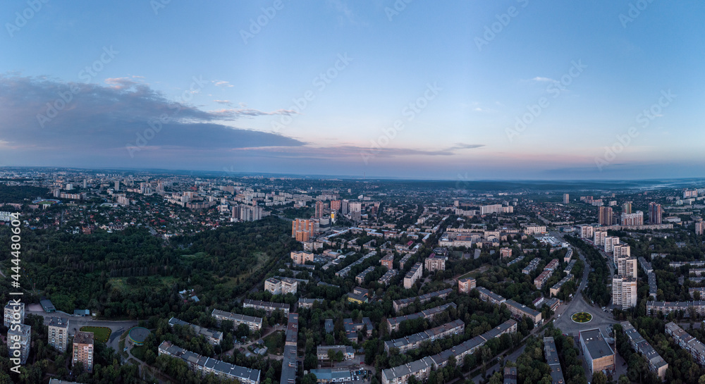 Aerial morning panorama view Kharkiv city Pavlove Pole district and Botanical garden. Multistory buildings near forest with scenic bright blue sky in summer dawn light