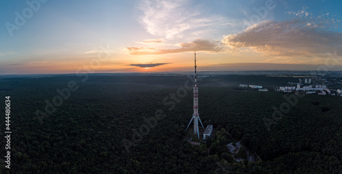 Aerial sunrise summer panoramic view on forest with telecommunication tower antenna and scenic dawn cloudy sky. Kharkiv, Ukraine