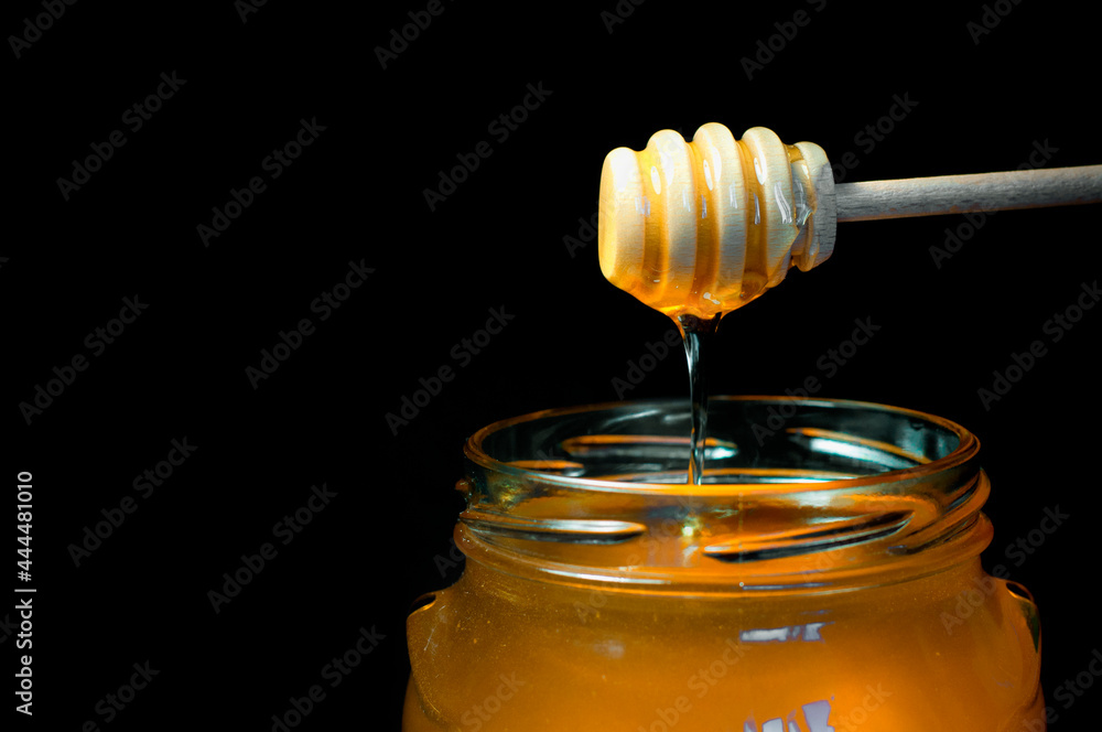 honey flows on a wooden spoon in a jar on a black background. High quality photo honey flows on a wooden spoon in a jar on a black background. High quality photo