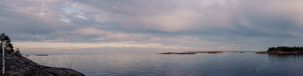 Panorama photo of the sunset in the archipelago in Sweden. Calm water and beautiful colors in the sky, reflecting in the sea. Summer evening on the coast with no people around.