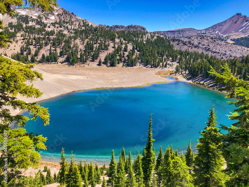 Clear blue alpine lake surrounded by fir trees and volcanic mountain peaks.