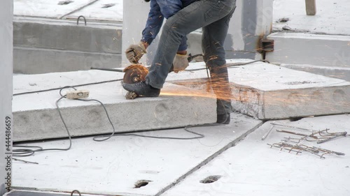 A professional builder cuts iron rebar with an angle grinder machine on a reinforced concrete slab at a construction site. Sparks fly from an electric circular saw. Construction of a new building.