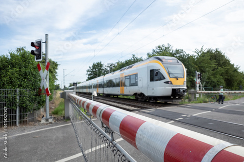 Selective focus view at red and white level crossing railway barrier which block the road and regional train move on the rail on countryside in Germany.	 photo