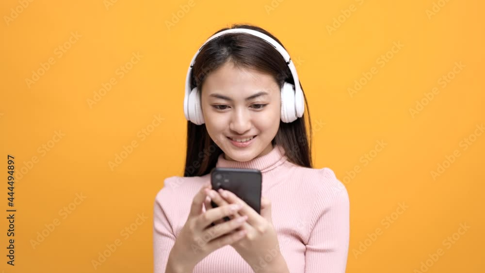 Beautiful young asian women choose song and play music from smartphone connection with wireless headphone having fun. Teenage girl listen to the music enjoy relaxing on isolated yellow background. Beautiful young asian women choose song and play music from smartphone connection with wireless headphone having fun. Teenage girl listen to the music enjoy relaxing on isolated yellow background.