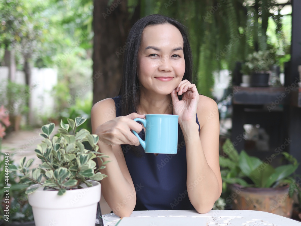 beutiful Asian woman with long hair sitting in the garden, holding blue cup of coffee, smiling and looking at camera. relaxing with morning coffee. beutiful Asian woman with long hair sitting in the garden, holding blue cup of coffee, smiling and looking at camera. relaxing with morning coffee.