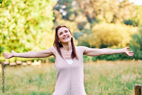 Smiling young adult woman with open arms in symbol of livertad in summer in a field or park photo