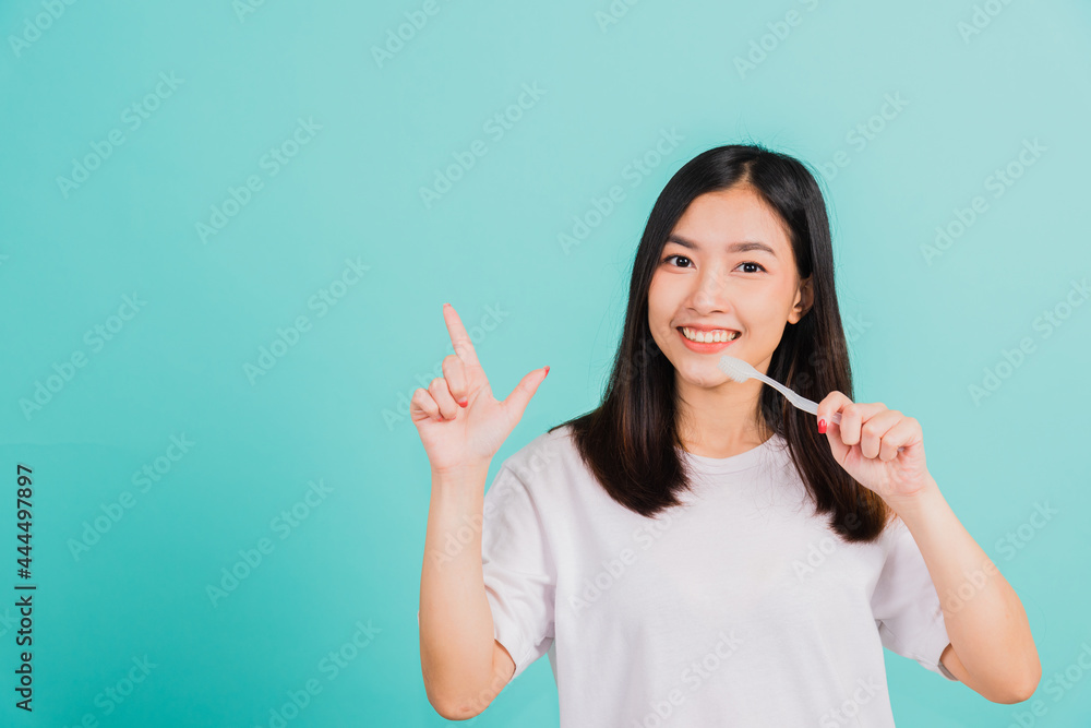 Portrait Asian beautiful young woman teen smiling holding toothbrush brushing teeth in the morning pointing finger to empty space studio shot isolated on blue background, Dental health concept Portrait Asian beautiful young woman teen smiling holding toothbrush brushing teeth in the morning pointing finger to empty space studio shot isolated on blue background, Dental health concept