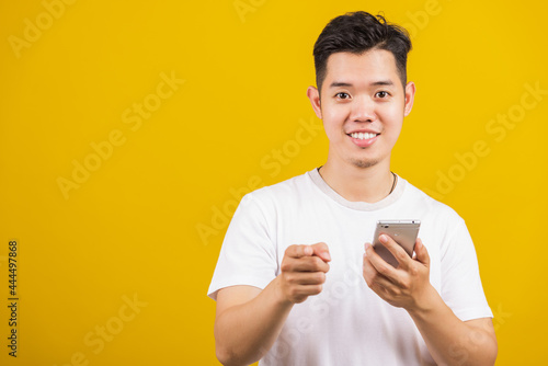 Asian handsome young man smiling positive holding smartphone blank screen and pointing finger to front, studio shot isolated on yellow background, making successful expression gesture concept