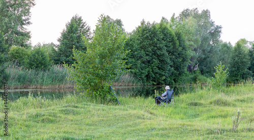 An elderly fisherman on the bank of a quiet river enjoys fishing.