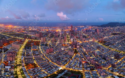 Aerial panorama of Kaohsiung City at dusk, a vibrant seaport in South Taiwan, with the landmark 85 Sky Tower standing among skyscrapers by the harbor and street lights dazzling under blue twilight sky