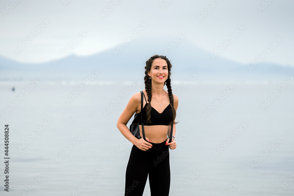 Girl traveler with a backpack on the beach, against the backdrop of mountains.