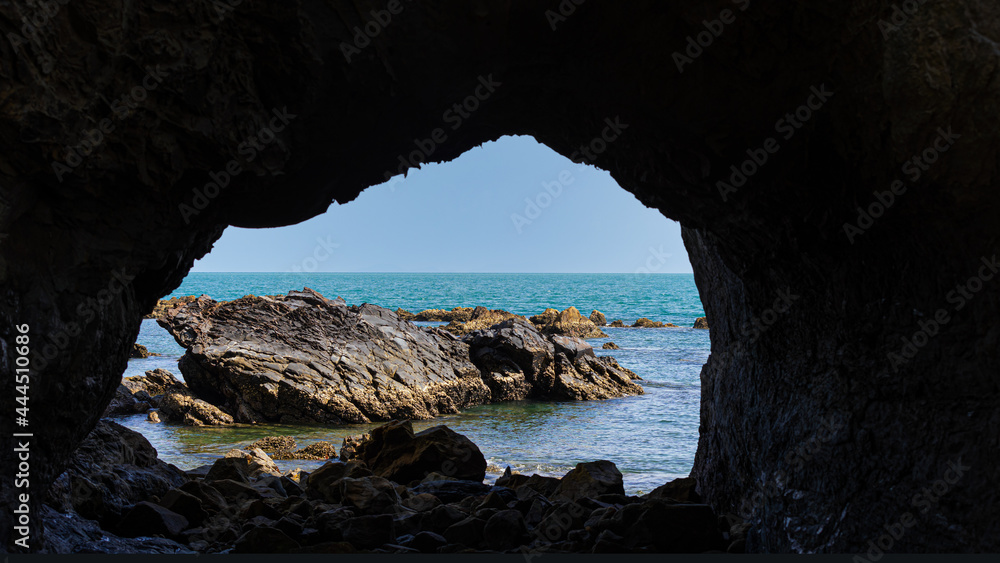 Framed shot of inside out from a cave next to the sea. Blue cloudy sky from inside the cave at a sea coast
