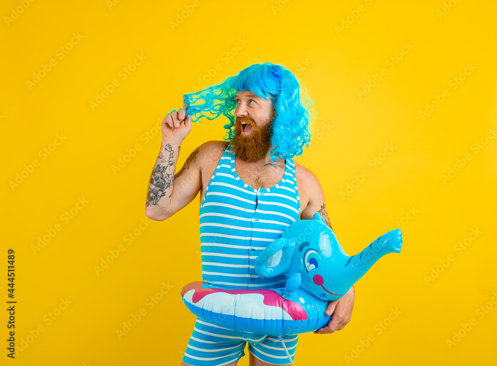 Happy man with life buoy, swimsuit and blue wig acts like a happy woman Happy man with life buoy, swimsuit and blue wig acts like a happy woman