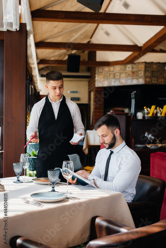 A young businessman in a fine restaurant examines the menu and makes an order to a young waiter in a stylish apron. Customer service.