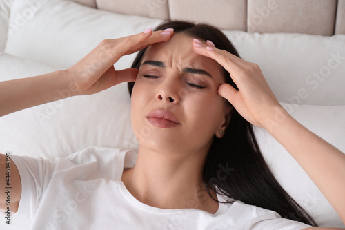 Young woman suffering from migraine in bed  above view