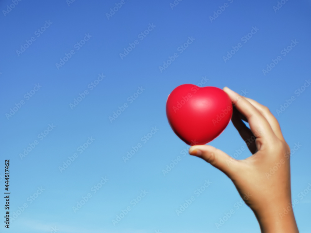 Selective focus hand holding red heart shape against blue sky. Love concept. Selective focus hand holding red heart shape against blue sky. Love concept.
