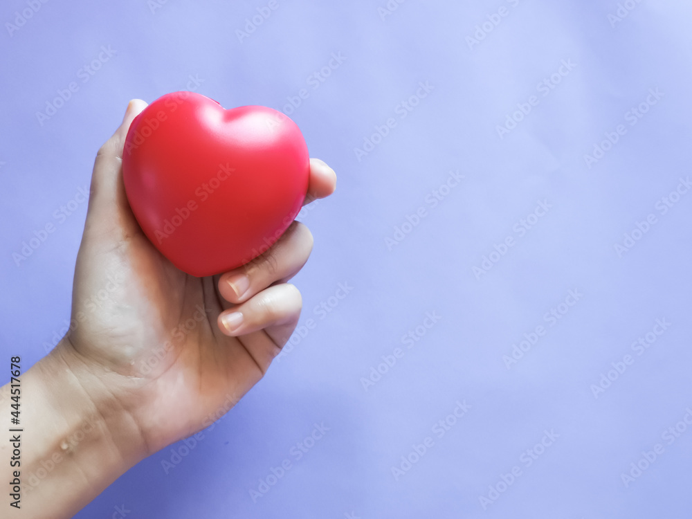 Selective focus hand holding red heart shape against purple background. Love concept. Selective focus hand holding red heart shape against purple background. Love concept.