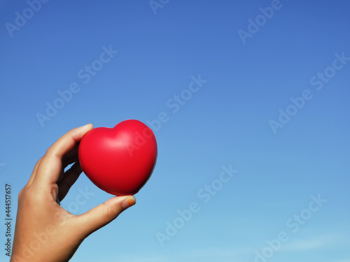 Selective focus hand holding red heart shape against blue sky. Love concept.
