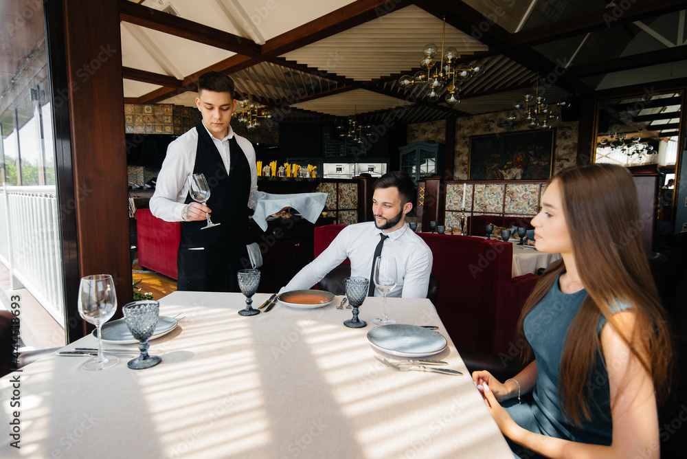 A stylish waiter serves a young couple who came on a date in a gourmet restaurant. Customer service in the catering. A stylish waiter serves a young couple who came on a date in a gourmet restaurant. Customer service in the catering.