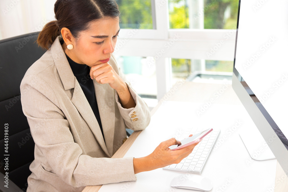 Young beautiful Asian woman using mobile phone and computer, working online at home. Checking smartphone while working. Young beautiful Asian woman using mobile phone and computer, working online at home. Checking smartphone while working.