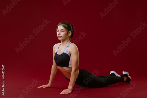 Young healthy caucasian woman in sportswear on a red background is engaged in fitness