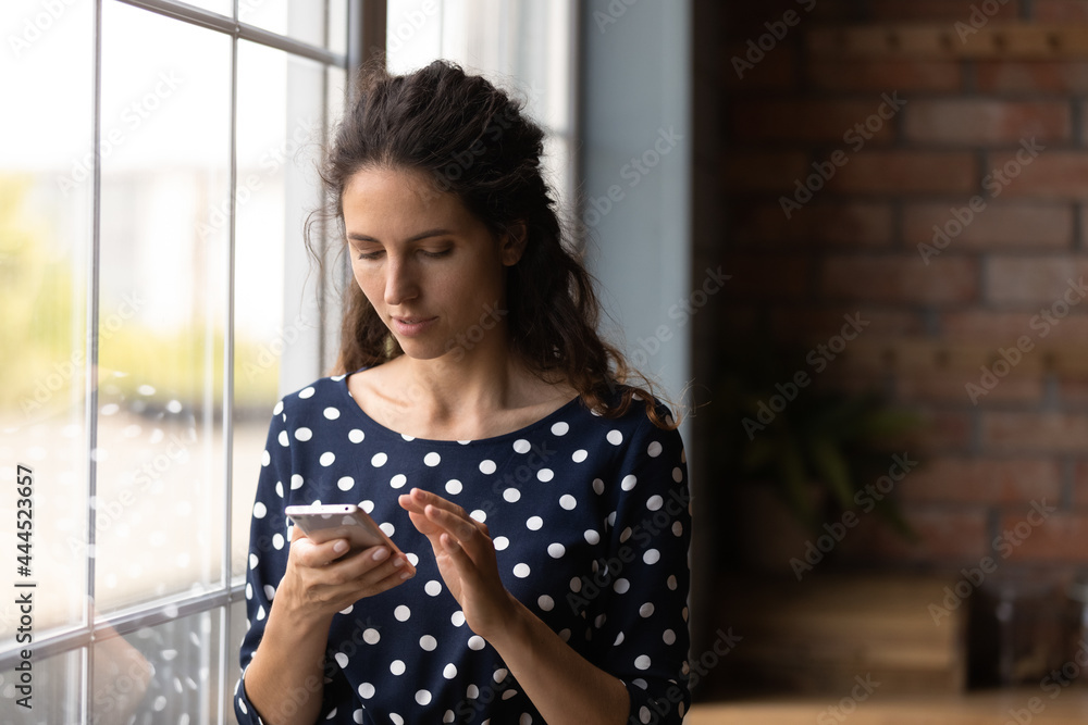 Serious young Latin woman using mobile phone at home, texting on virtual chat, ordering service via online app, making call, checking email, surfing internet, social media, reading blog article Serious young Latin woman using mobile phone at home, texting on virtual chat, ordering service via online app, making call, checking email, surfing internet, social media, reading blog article