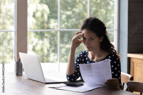Concern housewife checking utility bill, seeing mistaken too high costs. Worried woman reading paper invoice with doubt, having problems with loan, mortgage, taxes fee payment. Personal budget concept photo