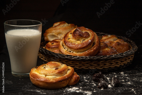 buns in a wicker bowl and a glass of milk on a dark background