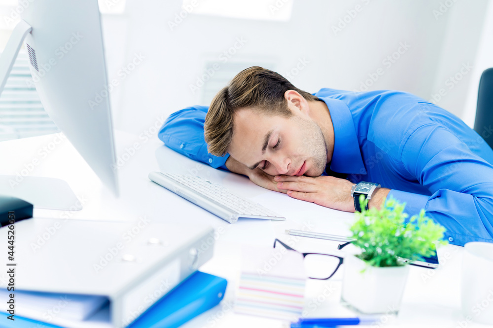 Obraz premium Image of very tired businessman in blue shirt, sleeping at workplace, with computer, indoors. Business, job and overworking concept.