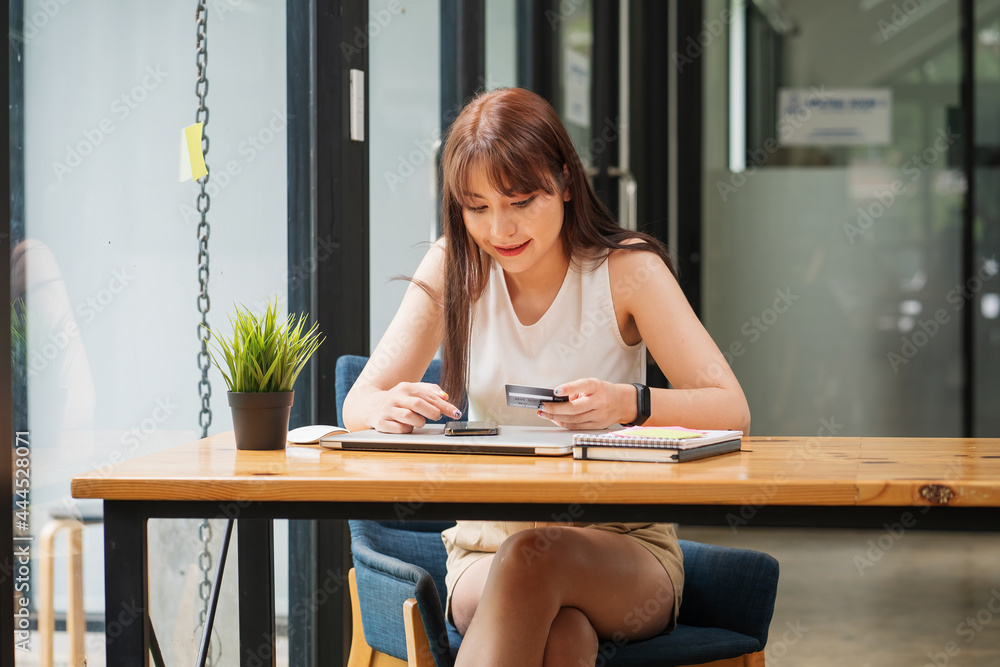 Young Asian woman using credit card and mobile phone for online shopping in coffee shop or coworking space, credit card mockup. Young Asian woman using credit card and mobile phone for online shopping in coffee shop or coworking space, credit card mockup.