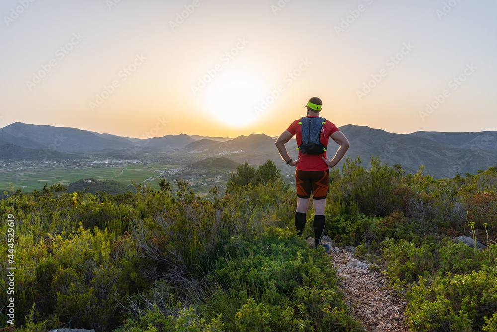 Man running down the mountain, at sunset, with the silhouette of the sun on the horizon.