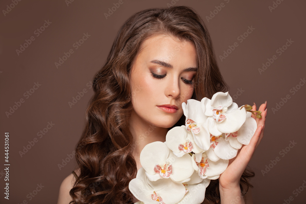 Healthy woman with clear skin, brown curly hairstyle and white orchid flowers. Facial treatment, hair and skin care concept