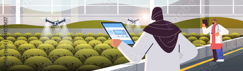 engineers controlling agricultural drones sprayers quad copters flying to spray chemical fertilizers in greenhouse
