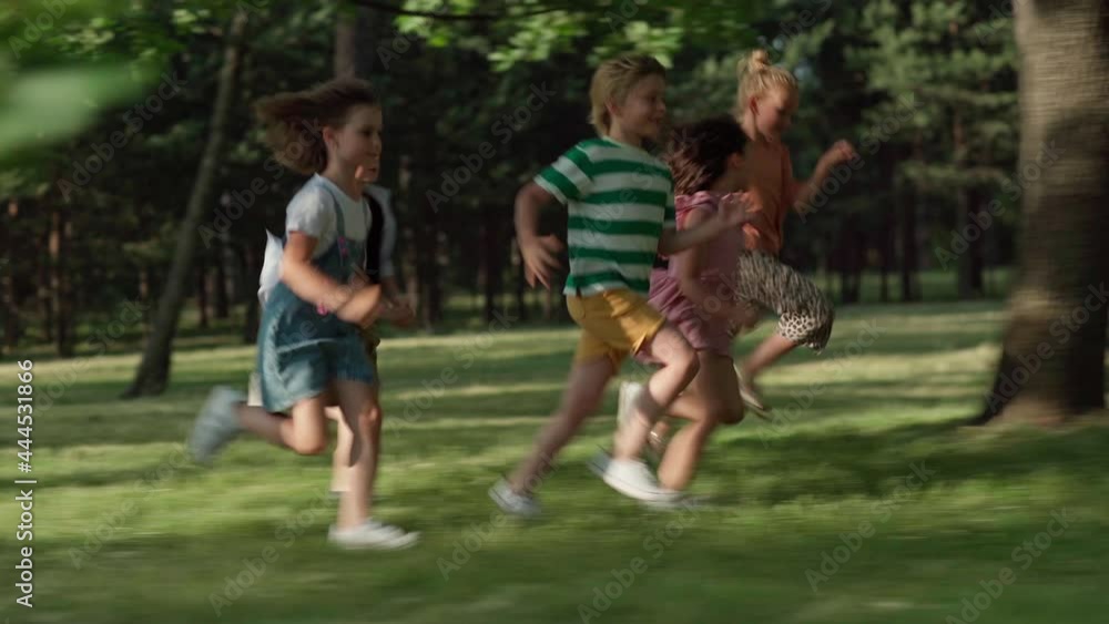 Side view of happy carefree kids running on green grass in park. Little friends having fun attempting to run faster than friends. Group of active children playing together Side view of happy carefree kids running on green grass in park. Little friends having fun attempting to run faster than friends. Group of active children playing together